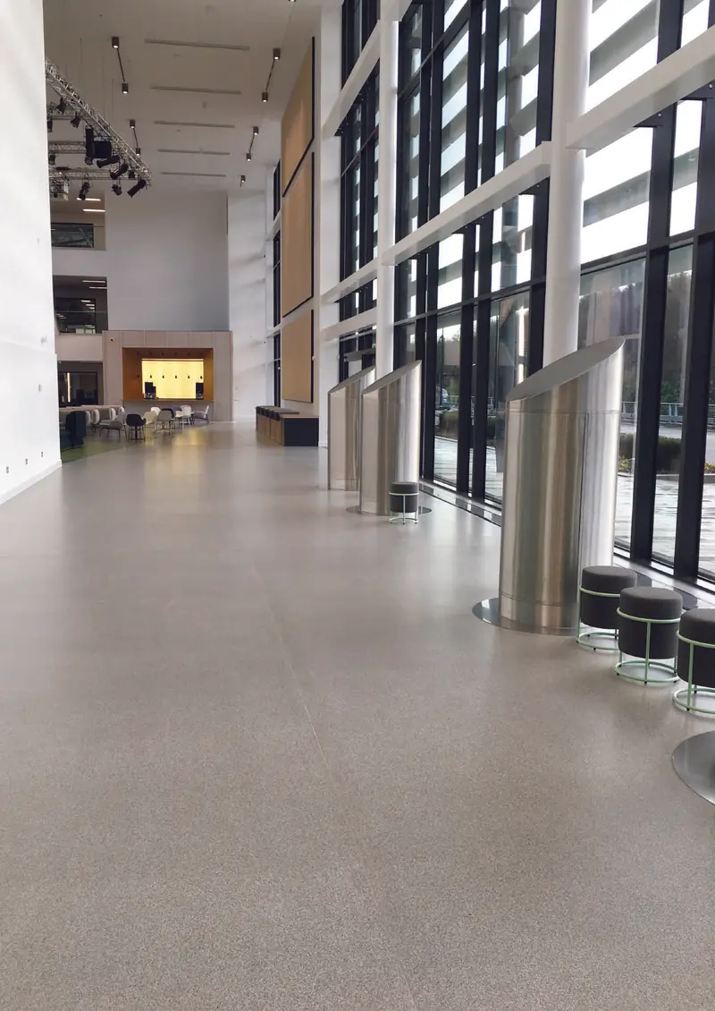 Hall d’entrée vitré au sol clair à paillettes, poubelles inox et banquettes