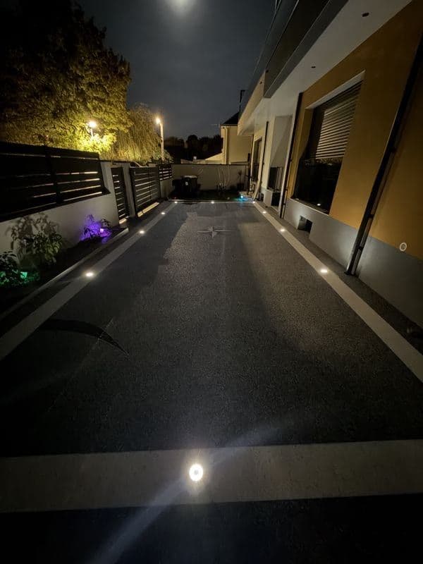 Cour en moquette de pierre éclairée de nuit par des spots encastrés le long des bordures